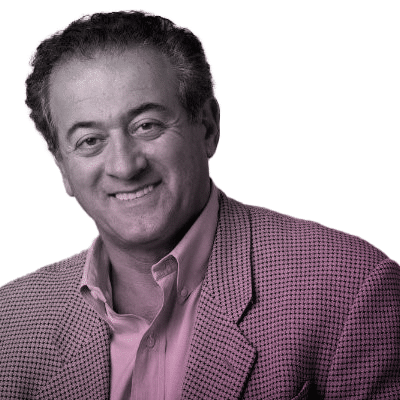 A man with short, curly hair smiles at the camera, wearing a checked blazer over a buttoned shirt against a white background.